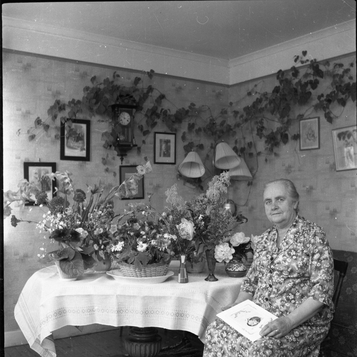Ester Palm sitter vid ett bord fullt av blommor, förmodligen en högtidsdag.