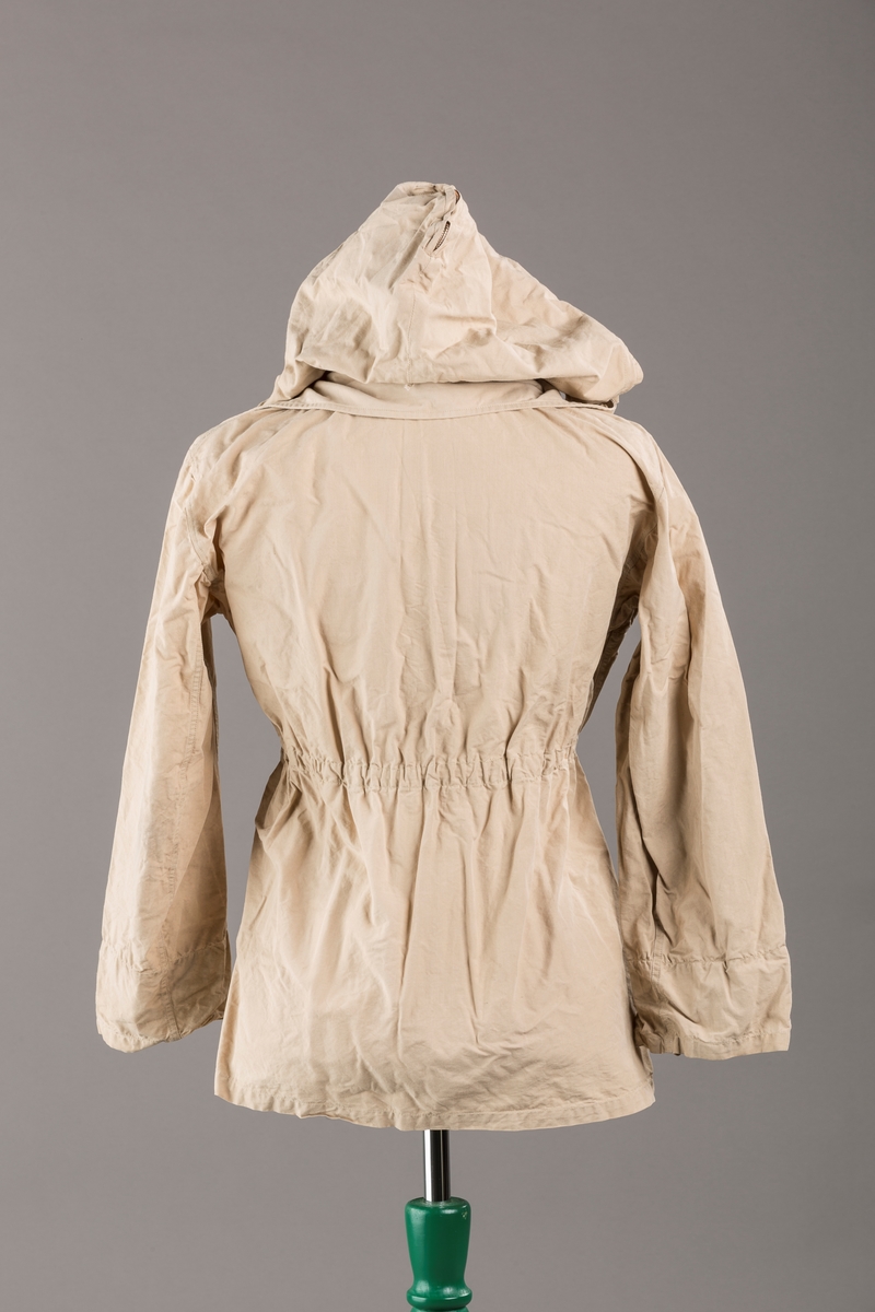 Form: Vanlig anorakkfasong med strikk i livet. 2 brystlommer med knapp.
Hette med glidelås på topp midt, snøring.
Glidelås helt ned foran.
Innermansjett med strikk i ermene.