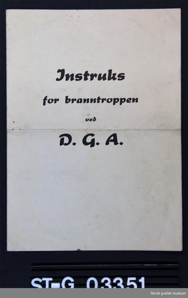 Et firesidig hefte med instrukser for branntroppen ved D. G. A. (Dreyer Grafisk Anstalt). Inni står det fylt ut navn på de ulike anvarlige under en utrykning.