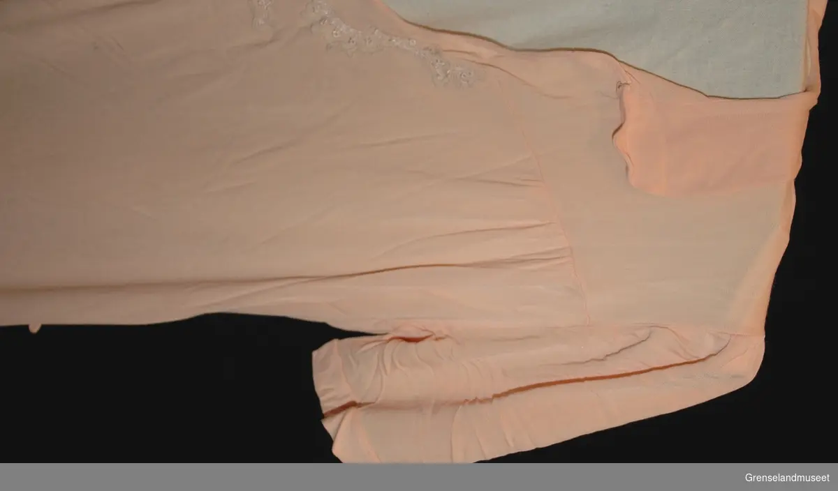 Lakserosa kunstsilke tricot, liten avrundet krave, Pyntet med maskinblonde rundt halsåpningen. Størrelse 46