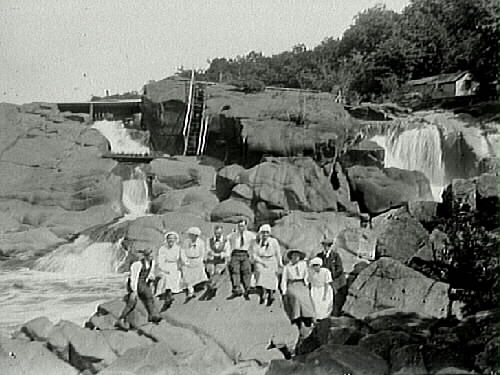 Fyra män och fem kvinnor på klippor mellan två vattenfall.