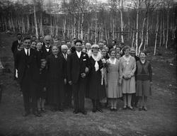 Brudepar med bryllupsgjester står ute ved bjørkelunden. Brud