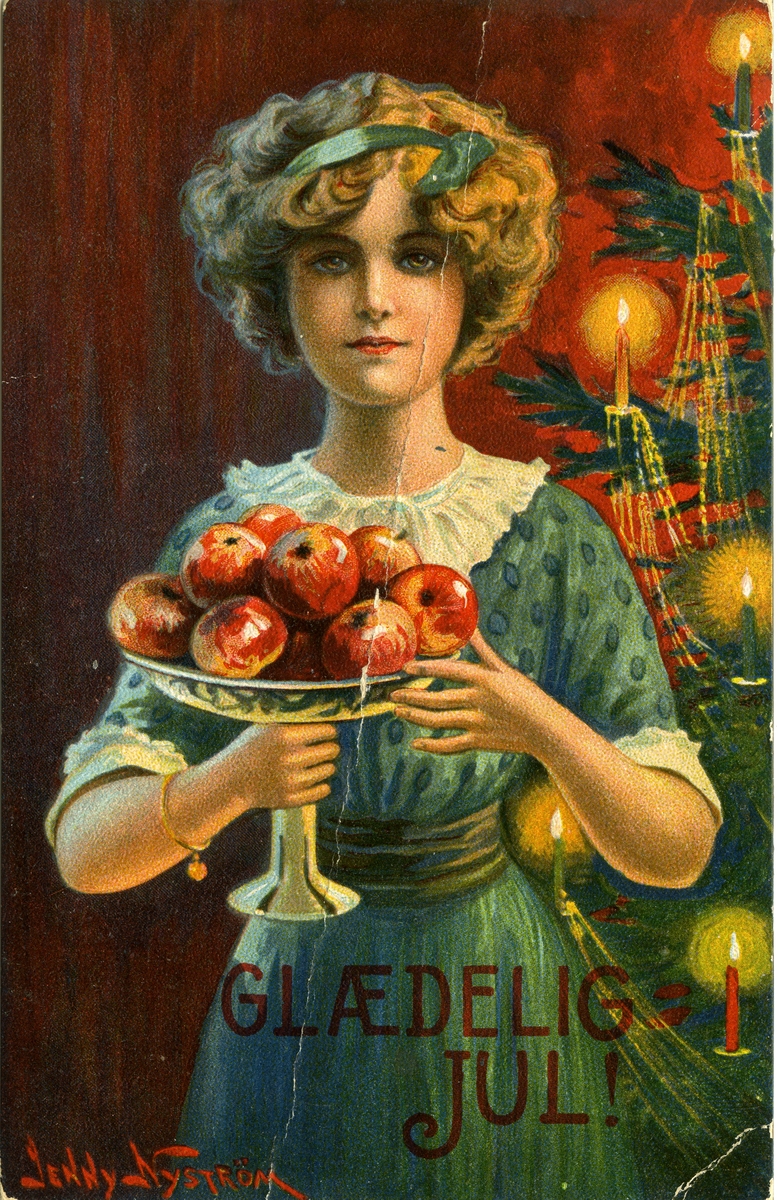 Julekort. Interiør stue. En ung kvinne bærer et fat med epler. Bak henne ses et juletre. Illustrert av Jenny Nyström (1854-1946). Datert 27.12.1917.