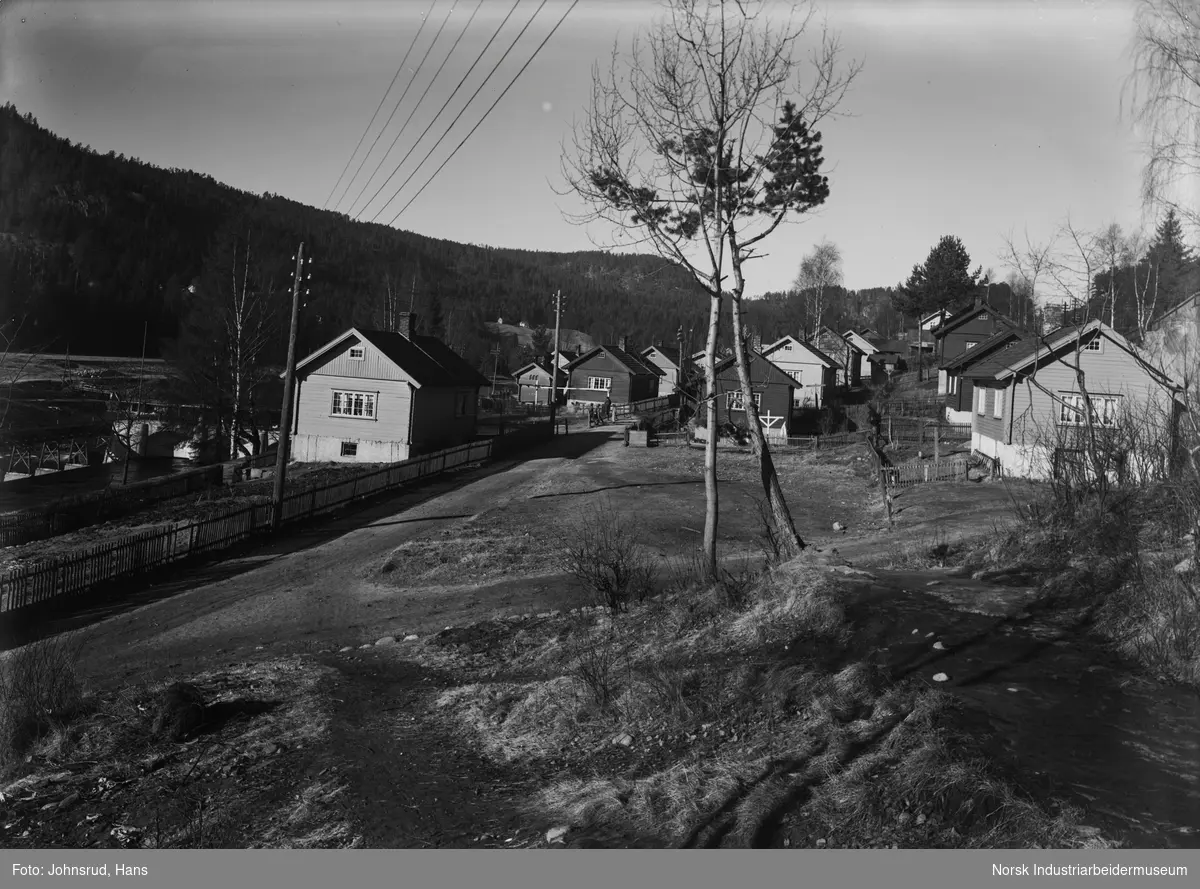 Boligområde ved Hyttebyen (Kanalbyen). Bolighus på begge sider av veien. Mennesker stående utenfor et hus.