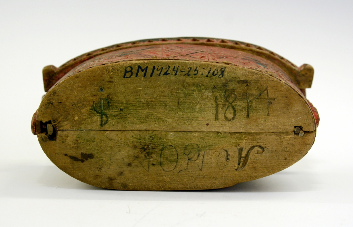 Tine av tre. Fra protokollen: Leikety-tine utskori i grovt kerbsnitt og plymrankkrullar. Under botnen skori 1814 og bokstavar. Standarane løglegt maksla som hovud med haarflettur. Raudmaala.