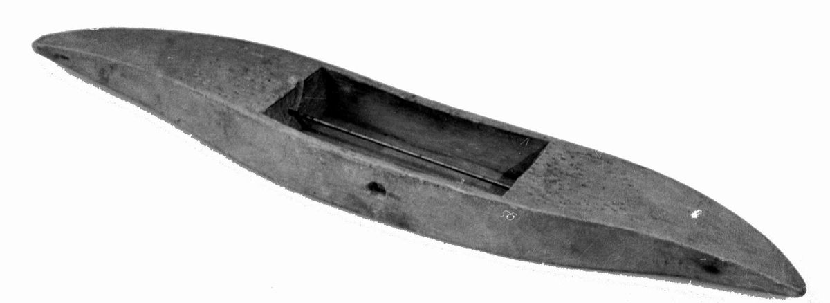 Avlang og buet vevskyttel av tre, med uthuling i midten der det er festet en trådspole av metall.