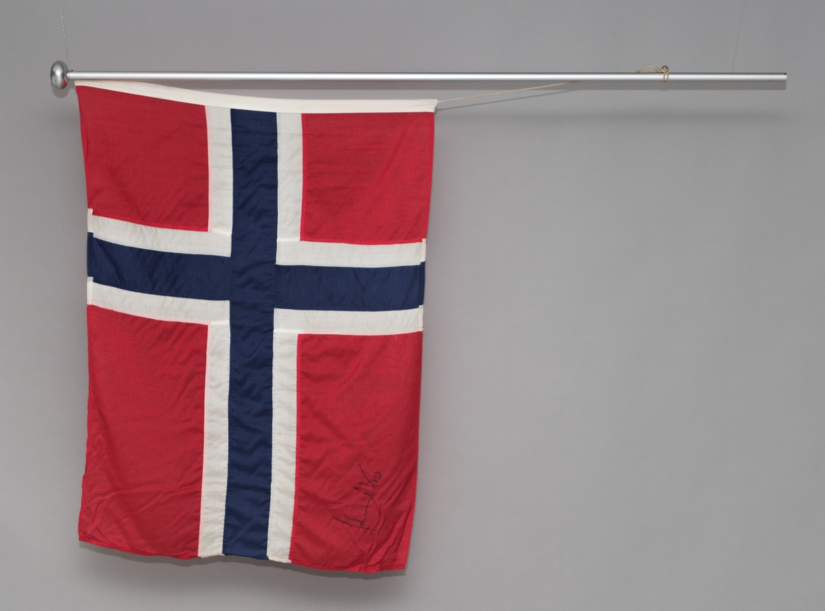 Norsk flagg med signatur av Johan Olav Koss. Flagget ligger en kartonghylse.