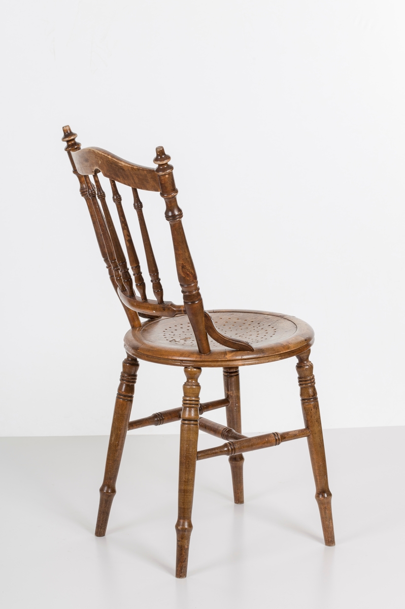 Stol i lakket treverk. Rundt stolsete med hullemønster. Rygg som er svakt buet med spiler og mønster. Dreide ben om spiler i rygg.