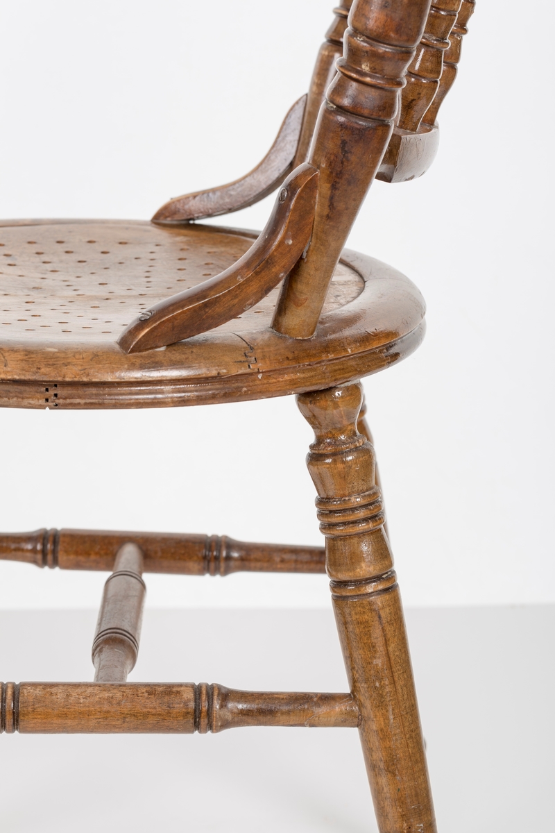 Stol i lakket treverk. Rundt stolsete med hullemønster. Rygg som er svakt buet med spiler og mønster. Dreide ben og spiler i rygg.