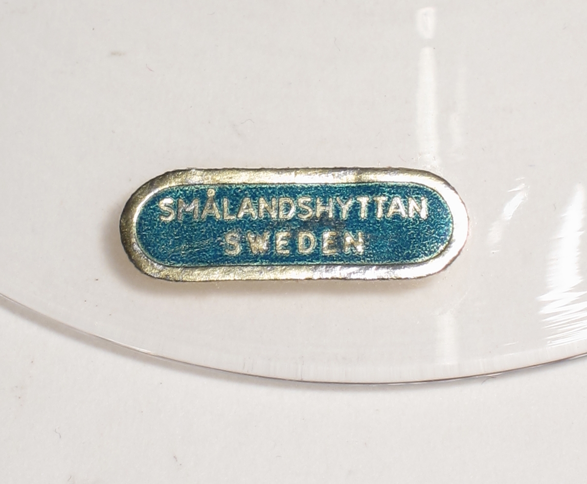 Vinglas med rundad kupa och högt ben som avslutas med en kulbats.
etikett: Oval med guldbård och blå botten "SMÅLANDSHYTTAN SWEDEN".