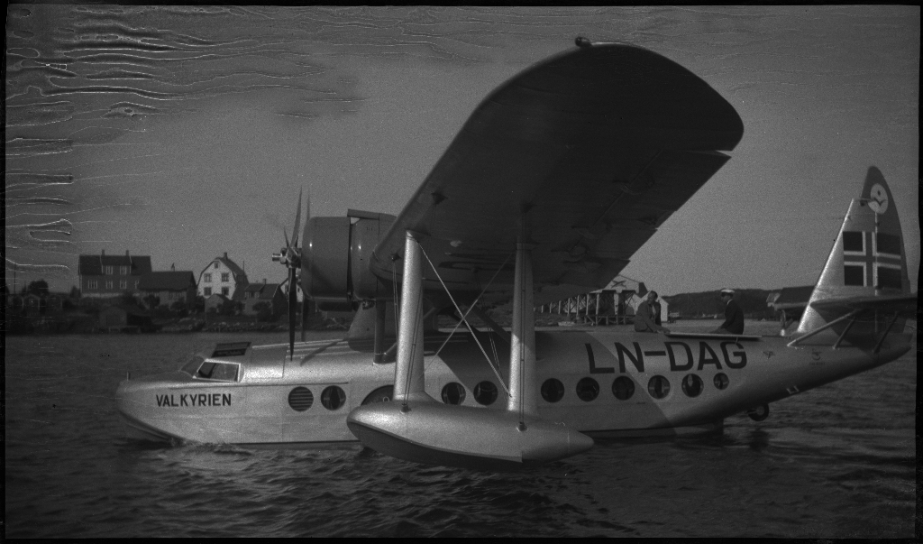 Bilder av Det Norske Luftfartsselskap sitt sjøfly (amfibie), "Valkyrien", som ligger på vannet. Registreringsnummeret, "LN-DAG", står på den bakre delen av flyet. En annen mann er med å besikte flyet.