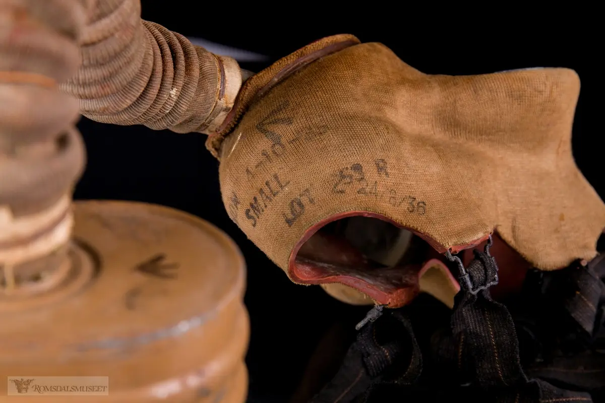 Britisk gassmaske brukt under andre verdenskrig. Ansiktsstykket består av tekstilbelagt gummi. En bøyelig slange går fra den runde, perforerte utlbåsningsventilen til et ovalt, tønneformet filter. Festestropper i gummi med bakhodestykke av lær.