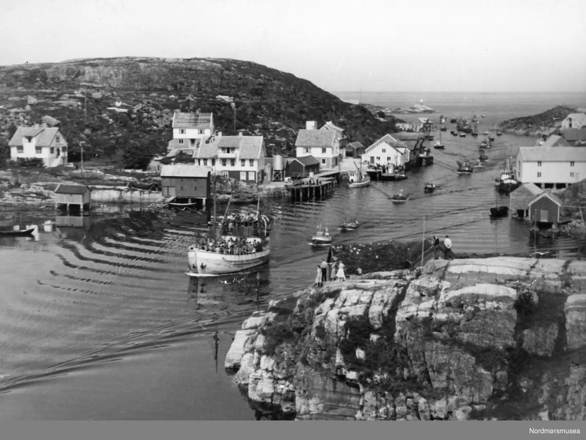 Foto av en rekke fartøy i Sveggen på Averøy kommune. Følget ledes an av en fraktebåt ved navn "Auken" hvis eier er John Haugenes. Det er kanskje Bremsnes sangerforening vi ser på båtdekket, muligens på vei fra Langøystevnet? Bildet kan trolig dateres til omkring 1956-1957. Fra Nordmøre museums fotosamlinger.
Foto av en rekke fiskefartøy på vei inn Sveggen i Averøy kommune. Legg merke til båten foran har dekket fullt av folk. Datering er trolig omkring 1920-1939. Fra Nordmøre museums fotosamlinger.