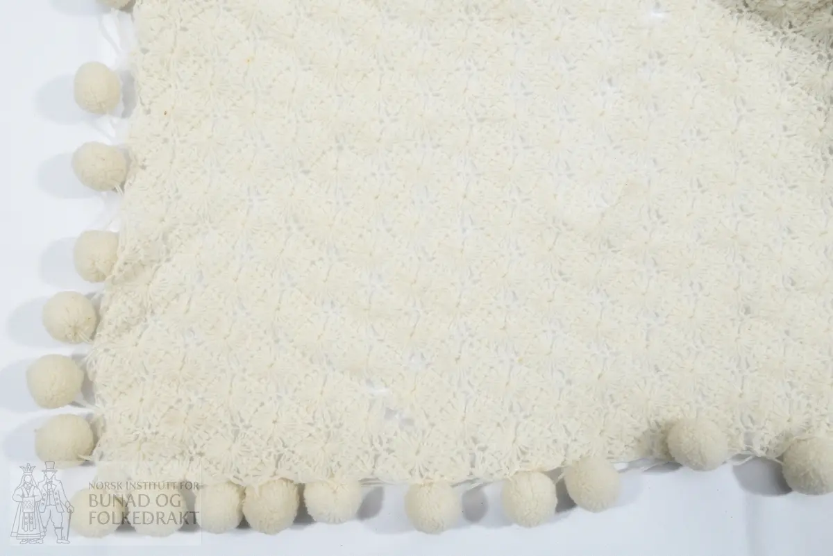 Skjerf. Heklet av tynt hvitt ullgarn. Med påsydde hvite pompomer hele veien rundt, også på kortsidene.