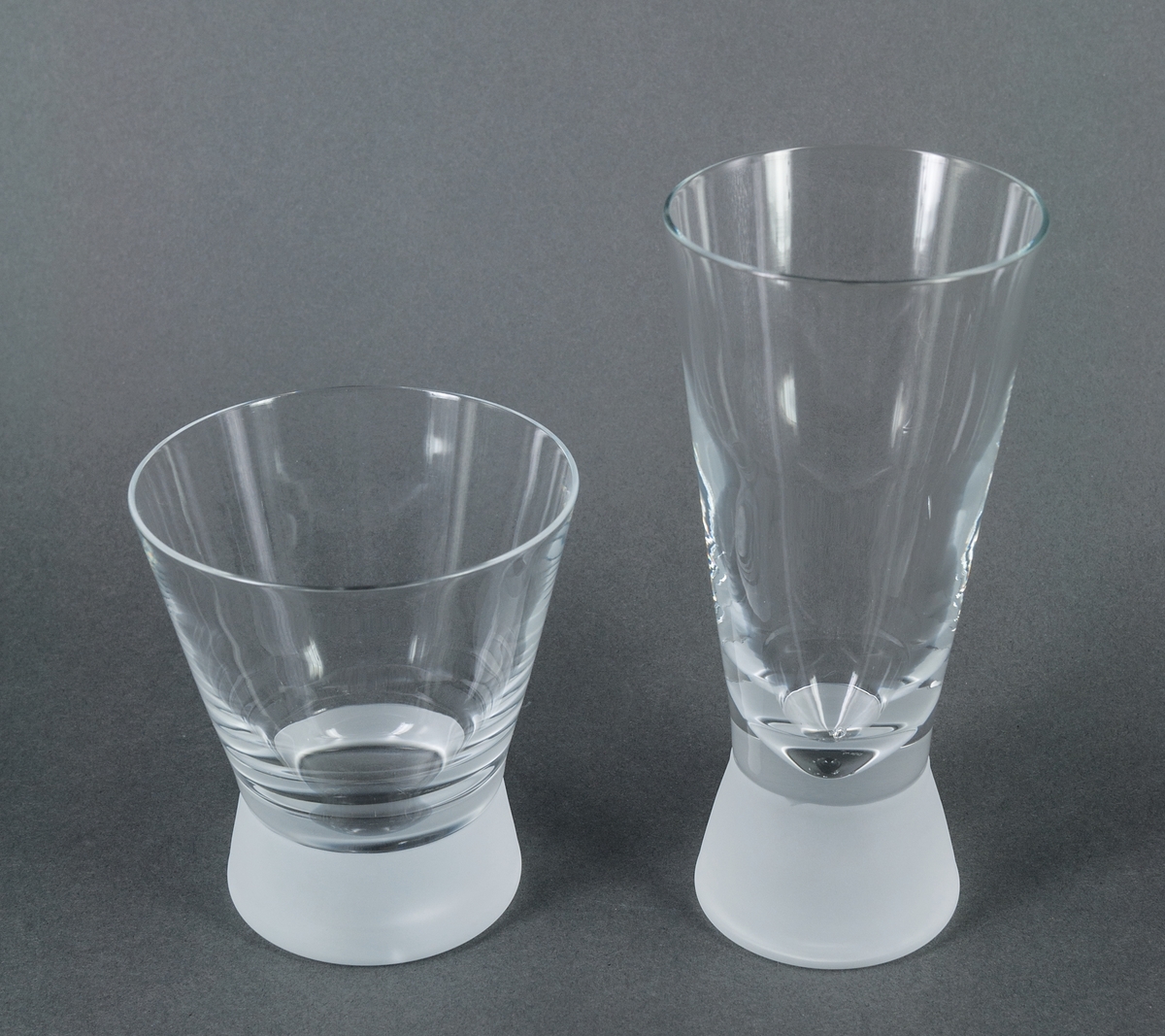 Cocktailglas (tumbler), prov till modell "Queen frostad". Ofärgat med tjock, frostad fot. Raka utåtlutande sidor. Design Gunnar Cyrén för Orrefors Glasbruk.