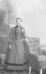 Ung kvinne står lent mot en lenestol. Nevnt som Kirsti Heen.