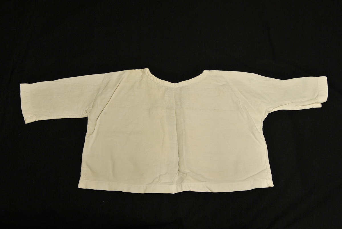 Undertrøye til spedbarn. Rektangulær i formen. Knytinger bak.