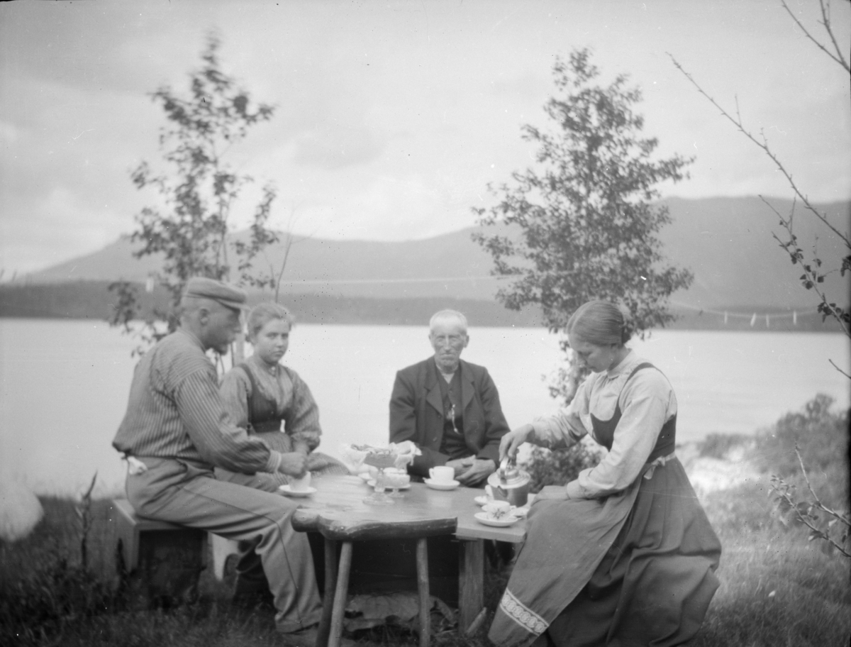 To kvinner og to menn ved kaffebord ute ved bredden av en innsjø