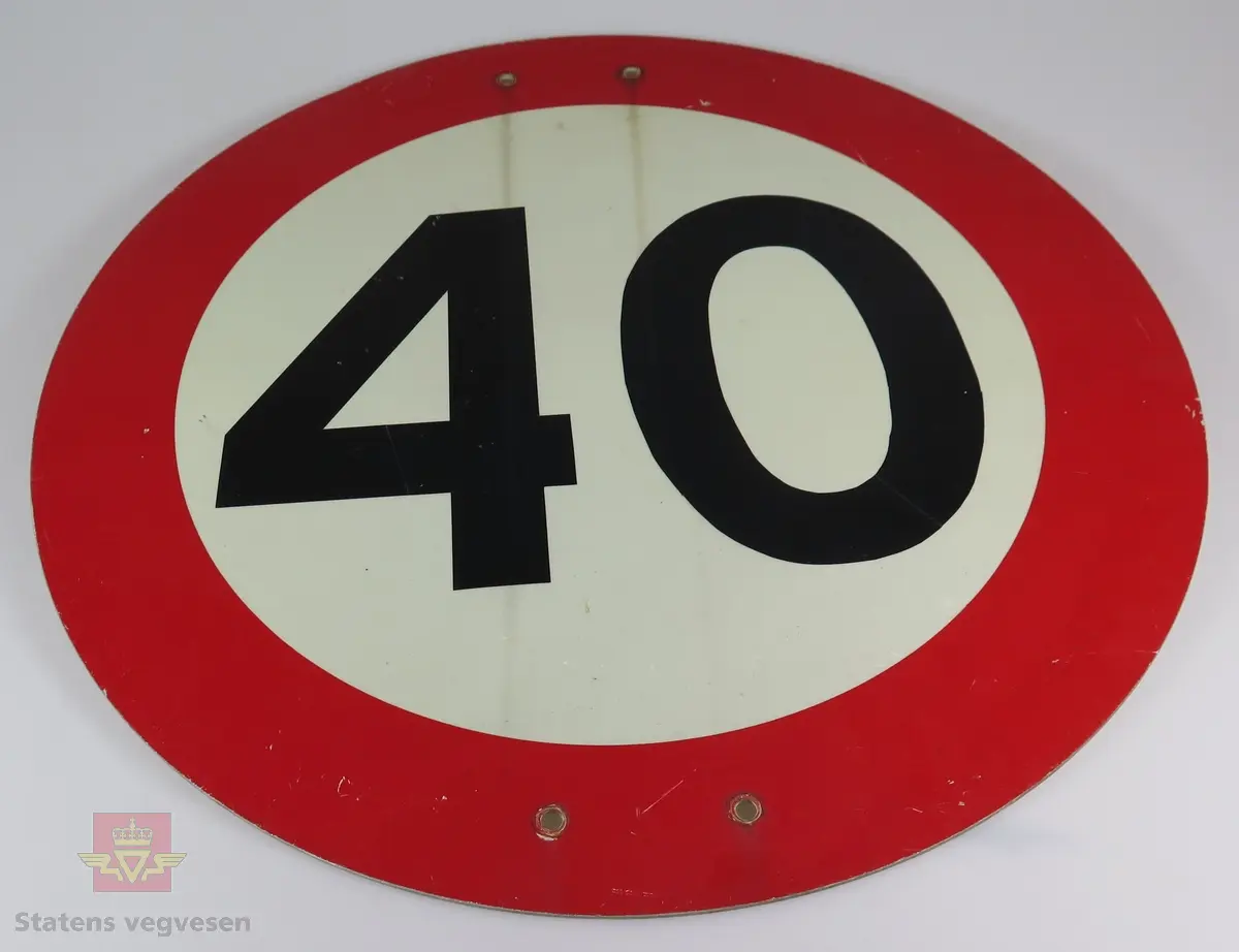 Sirkelformet skilt (stål plate) med fire hull for montering. Svart tall "40", på hvit lysreflekterende bunn. Rød bord. Grå bakside. Noe avskalling i fargen.