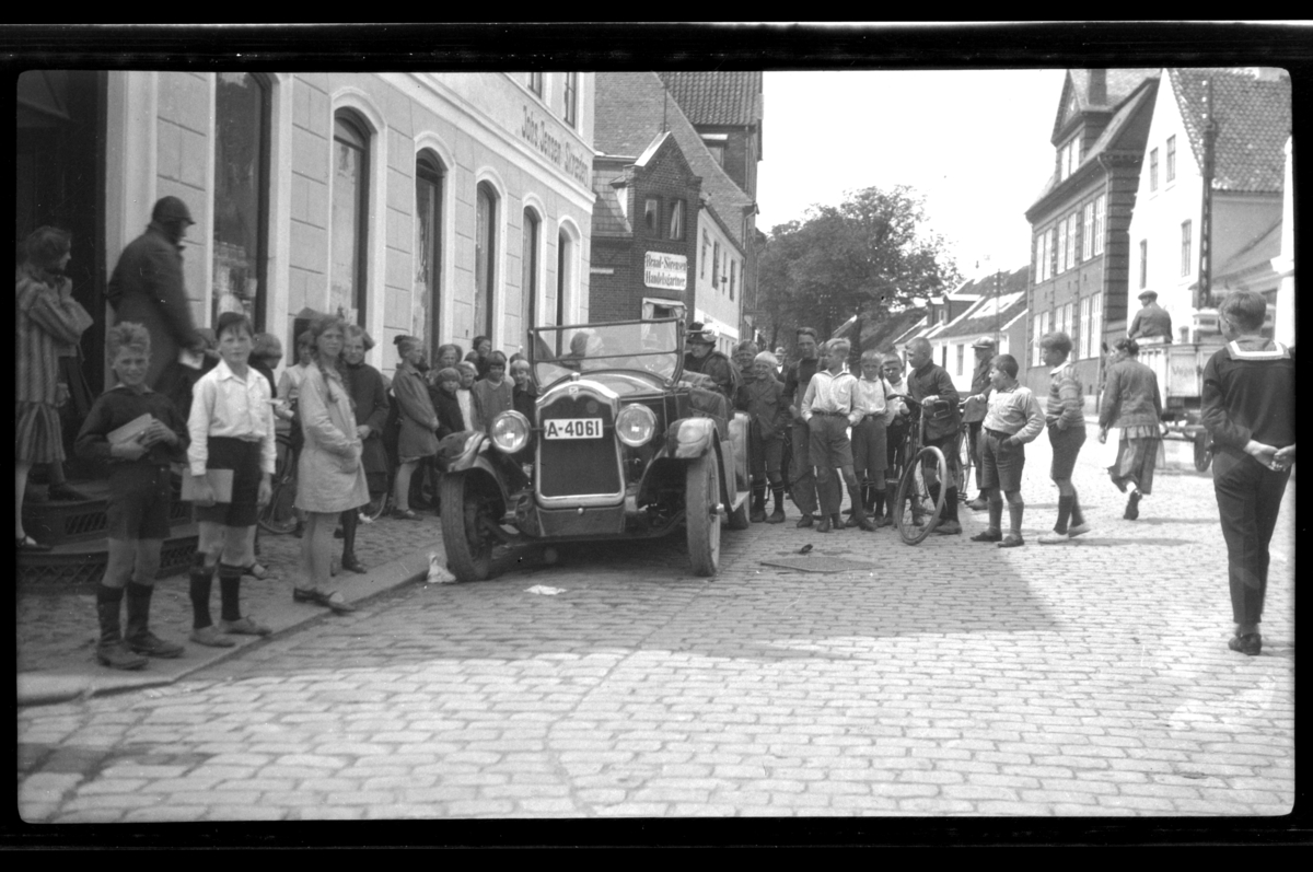 Mange barn står rundt Rolf Sundt sr.'s Buick i en dansk bygate. Fotografert 1927.