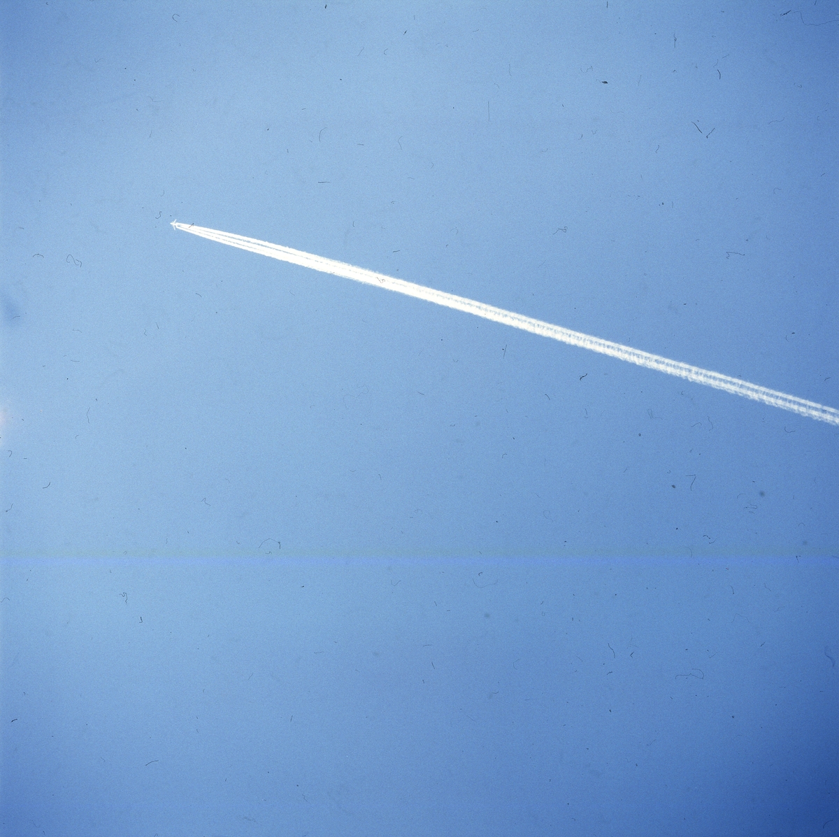 Ett flygplan lämnar ett vitt spår mot en blå himmel, Skåne 1 mars 1986.