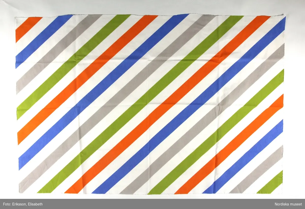 Mönster Avbilda, tryckta 5,5 cm breda diagonalränder i orange, grönt, grått och blått på vit botten.
Formgivare Tom Hedqvist.