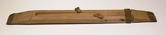 Vävspännare av trä, bestående av två delar där den ena delen är inskjutbar i den andra. Delarna fästs ihop med en sprint samt ett beslag av kopparplåt. Vävspännaren har ändbeslag av kopparplåt.