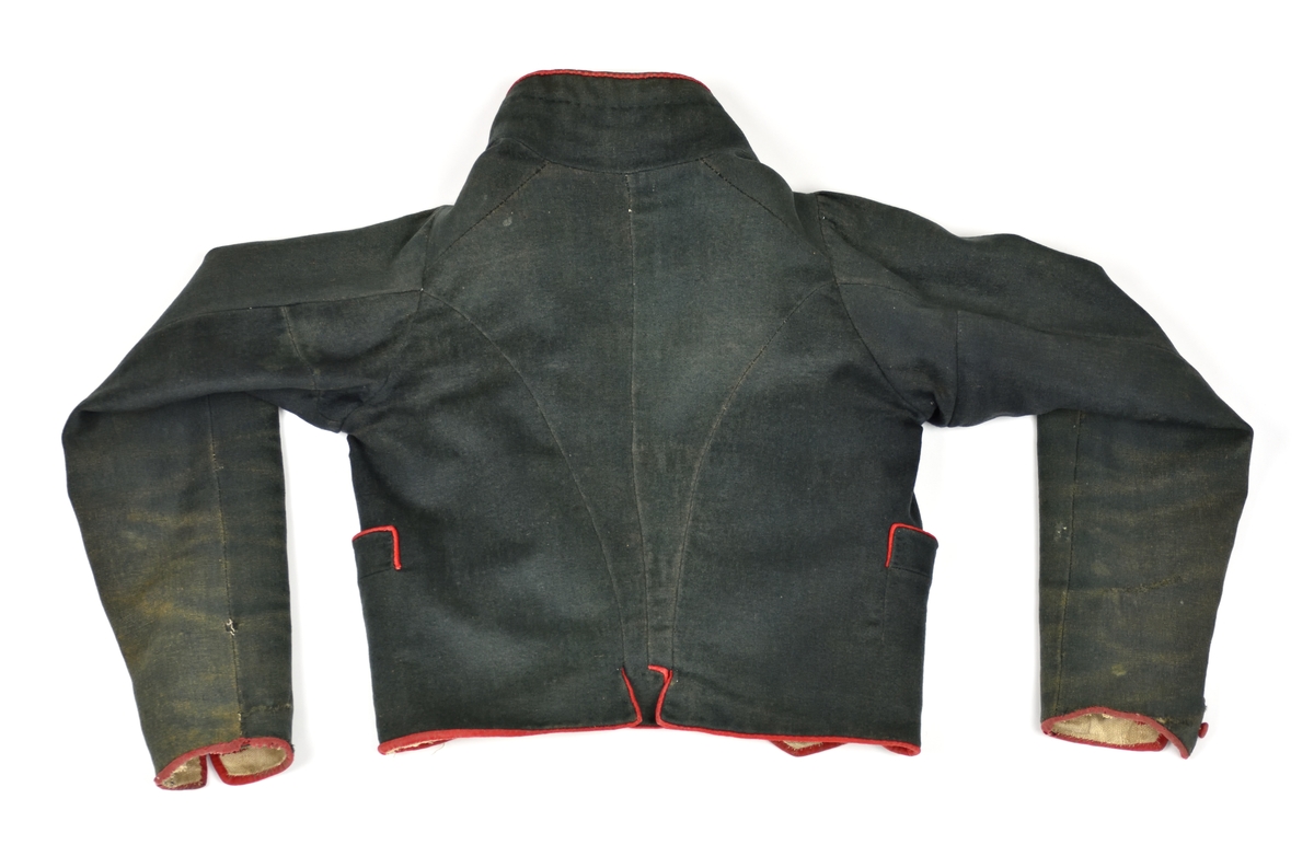 Svart handsydd jacka av svart vadmal med röda kanter och dubbelknäppning med åtta par tygklädda röda knappar. Jackan har linnefoder.
