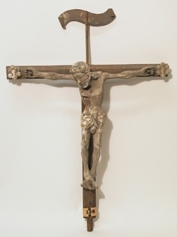 Korset i furu är utformat som ett T, möljigen från ett altarskåp eller sentida. På korsarmarnas ändar är trärosetter fastsatta och på en pinne sitter INRI-skylt. Figurens bemålning välbevarad.