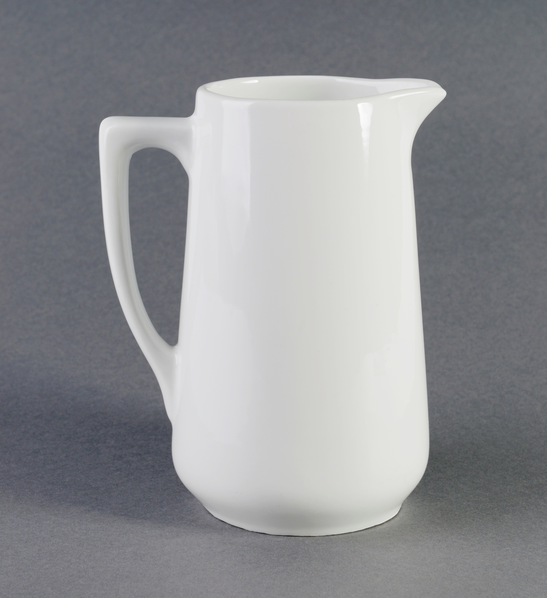 Konisk formet melkemugge av porselen med hank og glasur. Kan også ha blitt brukt som vannmugge.