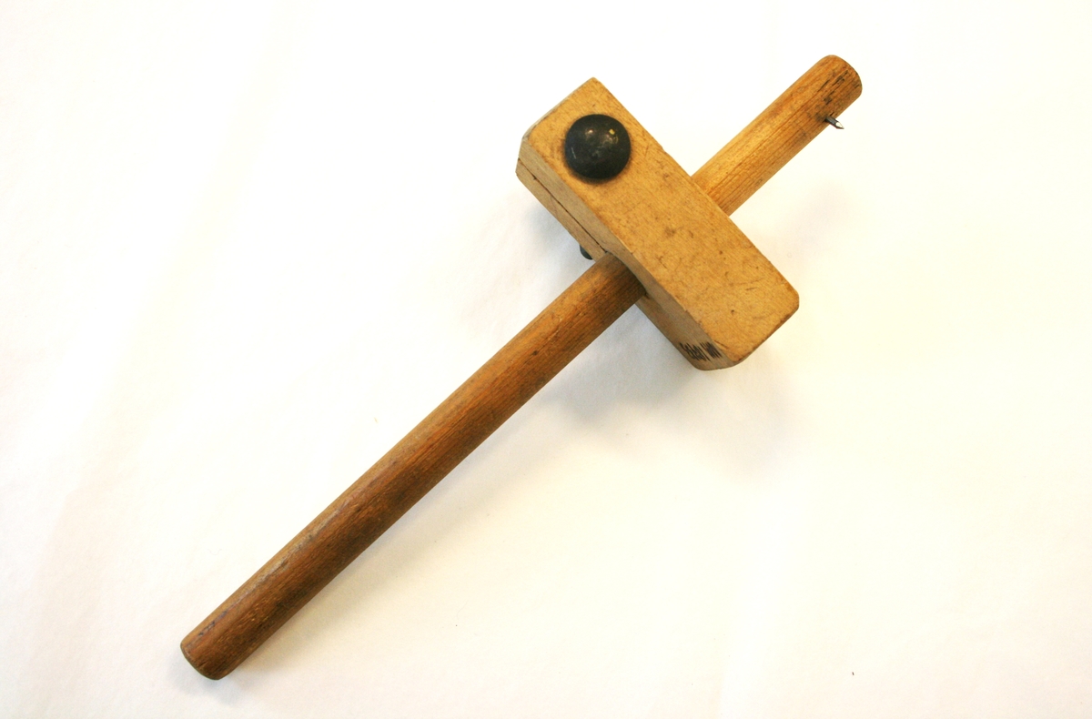 Stekmål i tre. Pinne med spiker i den ene enden, en kloss er festet med en liten tvinne og bolt i metall til å kunne justere avstanden fra markeringspinnen (spiker).