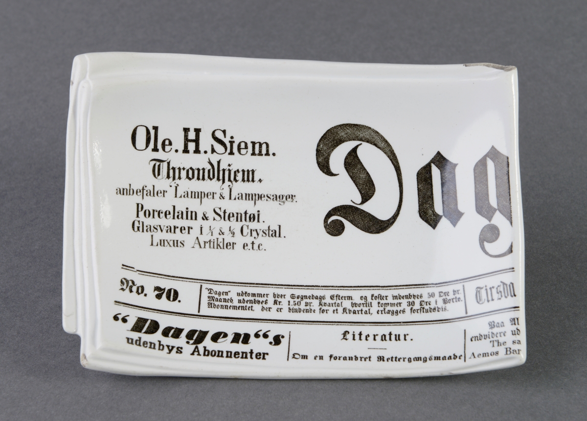 Rektangulært askebeger av glasert steintøy. Formet som en skål der hvor sigaretten skal plasseres, og det er deler av avisartikkel fra avisen "Dagen".