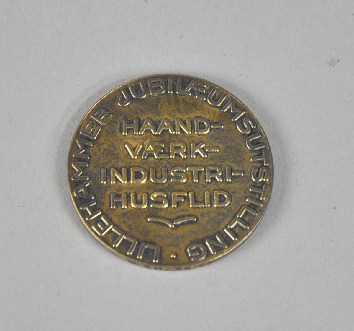 Rund medalje av bronse, med Lillehammer byvåpen i midten med laubærkrans rundt kanten. Tekst på baksiden.
