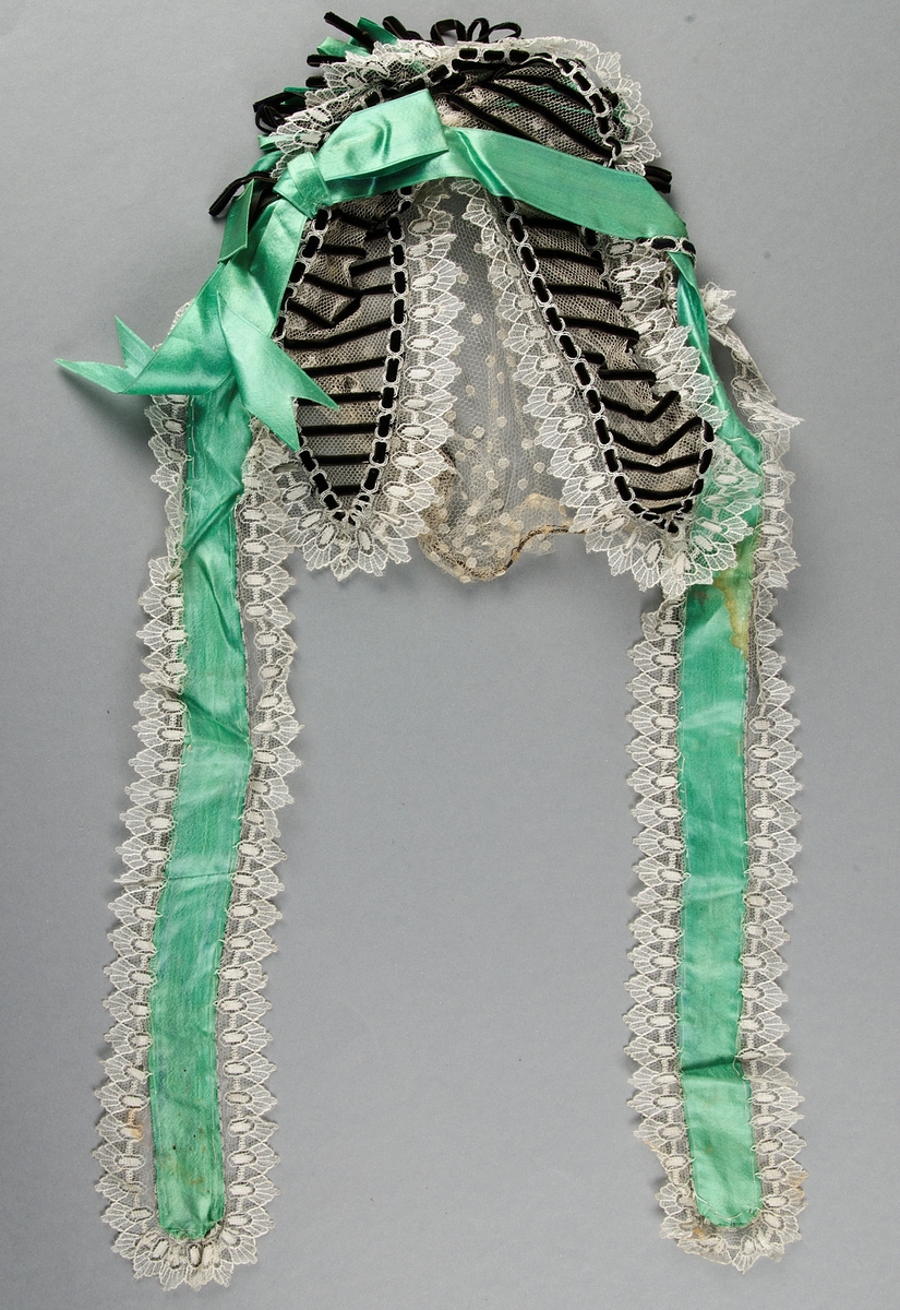 Hårklädsel 1800-1900-tal. Vit spets med band och rosetter i grönt siden och svart sammet.