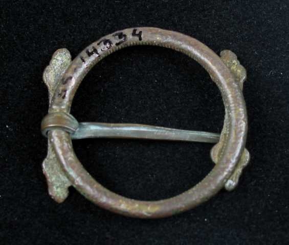 Hornring av messing med to pålodda stolper (horn). Stolpene er bueformede, midten er ringformet, mens endene er tungeformet. På hver tunge er det gravert fire "sirkeløyne". Ringen er formet av skruetråd.