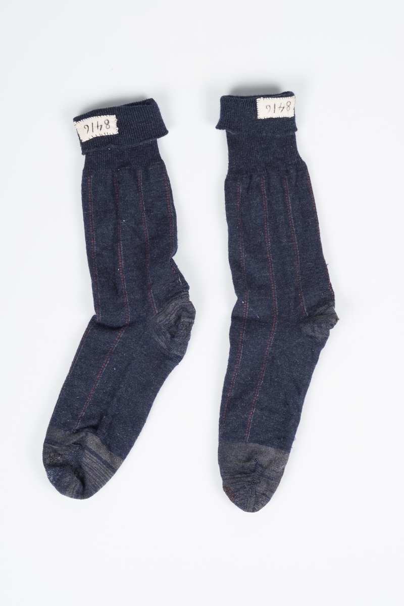 Mørkeblå høye sokker, med grå detaljer og røde og hvite striper. Sokkene er meget godt brukte og stoppet flere ganger. På innsiden øverst er det sydd inn en lapp med fangenummeret 8416, som identifiserer sokkene som Erich Mønnichen Plahtes.