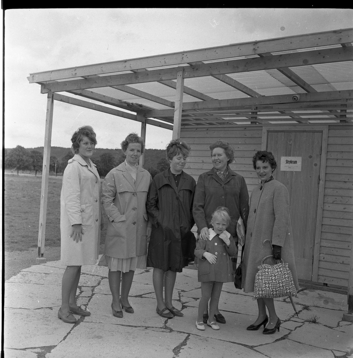 Fem kvinnor och en liten flicka stående framför en byggnad med strykrum vid Gränna camping. Fr vänster: Eva Heldebrandt, Alice Johansson och hennes dotter Birgitta Johansson samt Britta Blixt som har sin ena hand på en liten flickas axel. Kvinnan till höger är inte identifierad