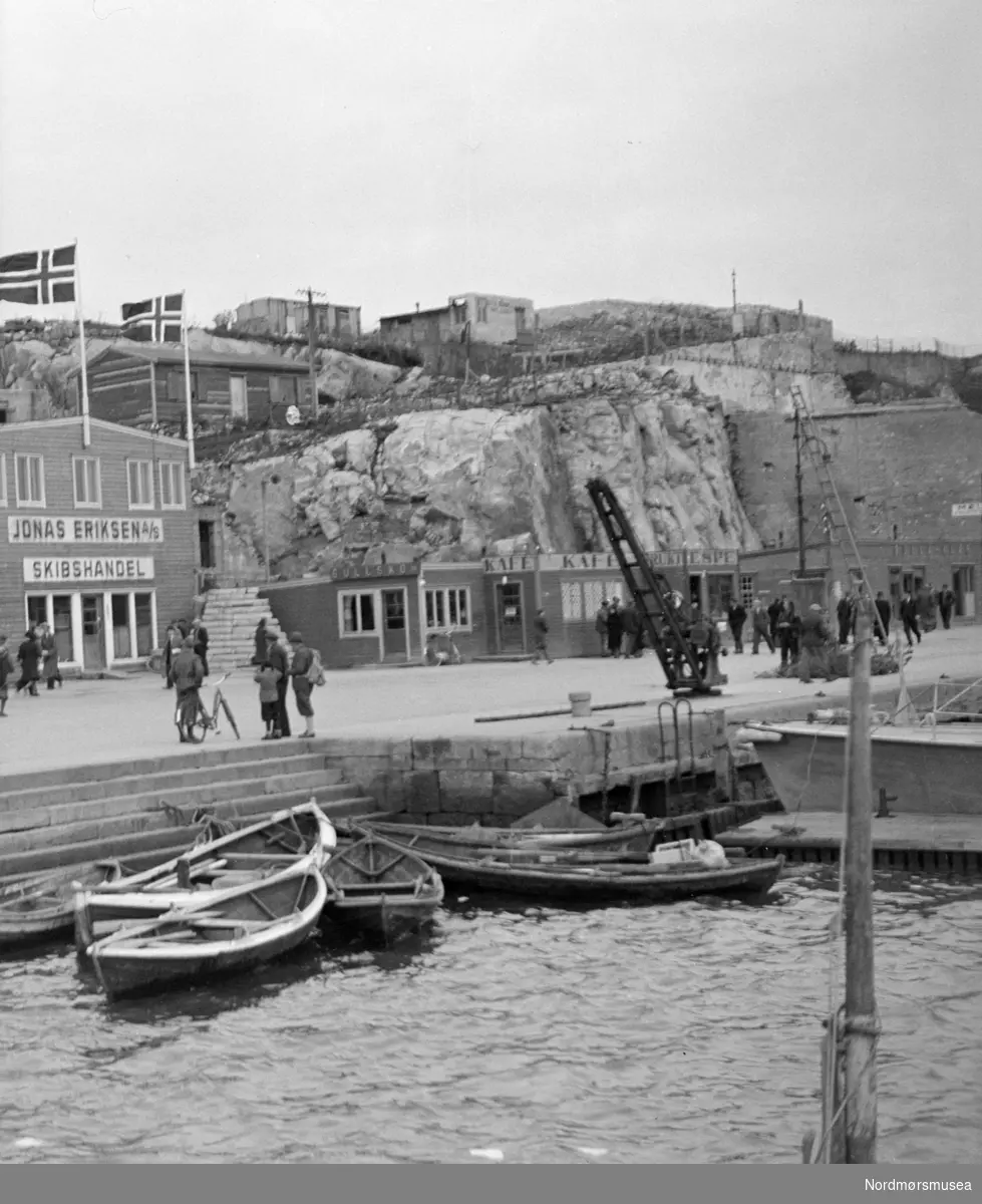 Foto fra en krigsherjet havneområde på Kirkelandet i Kristiansund, hvor vi bl.a. ser fisketrappa og brakken til Jonas Eriksen a/s skibshandel. Foto trolig fra maidagene 1945. Fra Sverdrupsamlingen ved Nordmøre museums fotosamlinger.