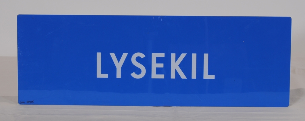 Destinationsskylt av ljusblå plast med texten "LYSEKIL" i vitt på båda sidor.