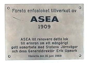 Skylt av rostfri plåt med svart text. Texten på skylten lyder:
"Första enfasloket tillverkat av
                  ASEA
                  1909
   ASEA lät renovera detta lok
   till erinran om ett mångårigt
gott samarbete med Statens Järnvägar
och dess Generaldirektör Erik Upmark
    Västerås den 16 juni 1969".