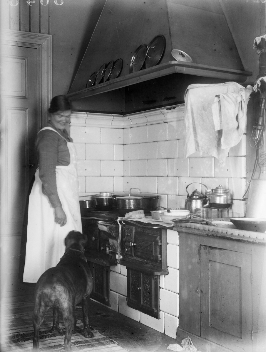 "Interiör från Eklunda gård, Lisa Holm i köket, hunden bakifrån", Simtuna socken, Uppland 1924