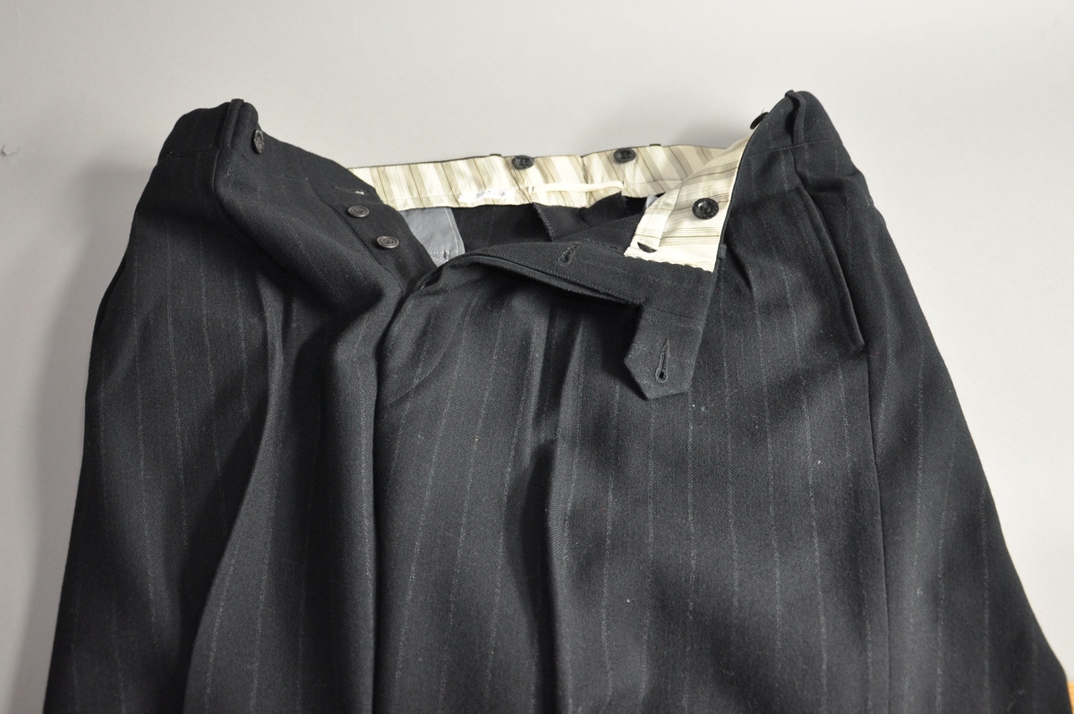 Dressbukse av mørk tekstil, med nedovergående hvite striper.
