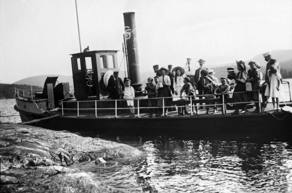 «D/S Porsgrund», fotografert i forbindelse med en lysttur til Kjeøya i Norsjø i Telemark, antakelig tidlig på 1900-tallet.  Fotografiet er tatt fra land, mot babord side av båten, som ligger mot ei bergflate, med en landgangsplanke fra rekka ved styrhuset mot den nevnte bergflata.  På akterdekket ser vi snaut 20 personer, de fleste barn, men også enkelte voksne.  De er kledd på en måte som tyder på at dette kan ha vært en søndagsutflukt.  D/S Porsgrunn ble bygd i 1867.  Opprinnelig fraktet dette fartøyet passasjerer på det stilleflytende elvepartiet mellom Porsgrunn og Skien.  Etter at den såkalte «Grevskapsbanen» ble åpnet høsten 1881 falt mye av markedet for dette transporttilbudet bort.  Snaut to år seinere kjøpte Skiensvassdragets Fellesfløtningsforening fartøyet med sikte på å kunne bruke det som tømmerslepebåt.  Yteevnen var imidlertid bare på 40 hestekrefter, noe som viste seg å være i knappeste laget.  Tidlig på 1900-tallet fornyet Fellesfløtningsforeningen mesteparten av sin dampslepebåtflåte.  I 1911 kunne man derfor selge D/S Porsgrund til en privatmann som ønsket å bruke den som bukserbåt.  Det faktum at fotografiet er tatt på Kjeøya, som var Skiensvassdragets Fellesfløtningsforenings eiendom, og at organisasjonens initialer fortsatt sto på skorsteinen, tyder på at dette fotografiet er tatt før salgstidspunktet. 