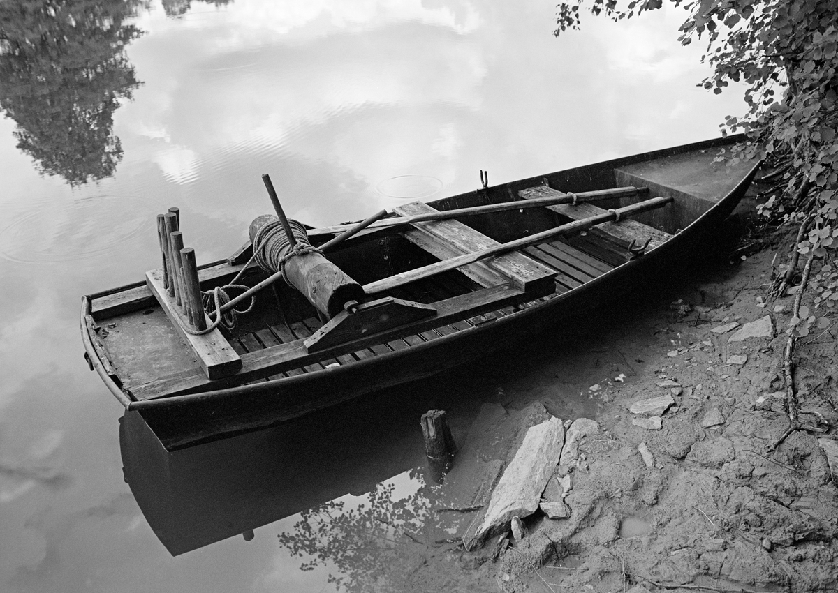 Såkalt «tjoreke» i Haldenvassdraget, fotografert ved en elvebredd i 1982.  Ei eike eller eke er en vanlig betegnelse på en trebåttype som ikke er bygd på en profilert, nedstikkende kjøl, men med et bord som midtakse. I dette tilfellet kan det imidlertid synes som om eka har hud av tynne stålplater.  «Tjor» er betegnelsen på et vindespill som er montert oppi båten, og som ble brukt til å trekke sammen tømmer ved slusene.  Det besto av en horisontal, sylindrisk trekabbe som det var tappet pinner, såkalte «horn» inn i, og viklet 6 millimeters tau rundt.  I begge ender av den nevnte kabben var det tappet inn jernteiner, som ble festet bak J-formete jernbeslag på treklosser oppå den ramma tjoret kvilte på.  Bakerst på den samme ramma, over aktertofta, var det påspikret et kraftig tverrtre med nedtappete pinner.  Tjoret ble brukt til å trekke fløtingstømmer med.  Båtkaren satt da aktervendt i båten og roterte kabben ved å dra hornene på oversida mot seg.  Han kunne også bremse eller låse posisjonen ved å sette beina mot horn på undersida av kabben.  Pinnene akterut ble brukt til å styre vinderetningen med.

Pensjonert direktør Tore Paulsen-Næss fortalte følgende om ekebygginga i et brev han sendte Norsk Skogmuseum med informasjon om ei tjoreke Haldenvassdragets Fellesfløtingsforening overdro til museet (jfr. SJF.07890):

«Fløtningsforeningen hadde egen smed på Ørje fra 1908. I sommerhalvåret arbeidet han som maskinist på et av moseapparatene. Om vinteren bygget han eker og hadde vedlikeholdet av mosemaskinene. Det ble bygget en egen slip som kunne trekke opp moseapparatene for vedlikehold. Smeden var Johan Iversen (1883-1962). Han sluttet ved fylte 70 år 9. 5. 1953, men hjalp til noe i 1954 og i 1955. Nødvendig vedlikehold av de dampdrevne moseapparatene ble utført av andre maskinister. Det var etter hvert anskaffet mindre, motordrevne varpebåter og buntemaskiner. I 1955 ble det ansatt en motorkyndig verkstedformann på Ørje, Kåre Granli (1921-1991). Han påtok seg også bygging av eker, og ble satt inn i jobben av Johan Iversen. Granli bygget de siste ekene i 1959. Ekebyggingen og vedlikeholdet ble overtatt av Johan Furulund, som var fast ansatt i Fløtningsforeningen 1960-1972. Han arbeidet som båtfører i fløtningstiden, og som hjelpearbeider i verkstedet i vinterhalvåret. Han fortsatte med dette arbeidet etter at han ble ansatt som slusemester.»

En liten historikk om tømmerfløting og kanaliseringsarbeid i Haldenvassdraget finnes under fanen «Opplysninger».