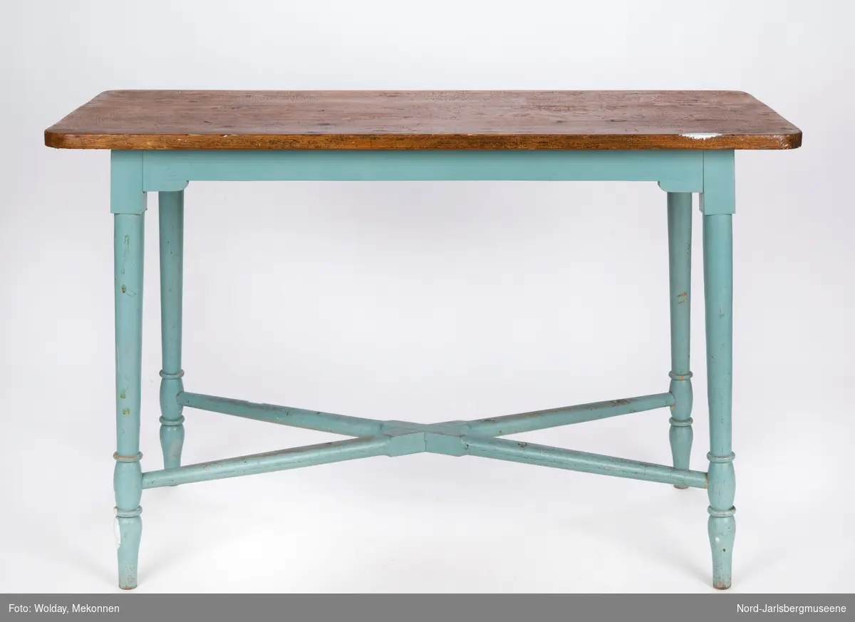 Et bord, kjøkkenbordtype, med lakkert bordplate og blåmalte ben og understell. Bena har dreid dekor, og er stabilisert ved et kryssverk nederst mellom de fire bena.