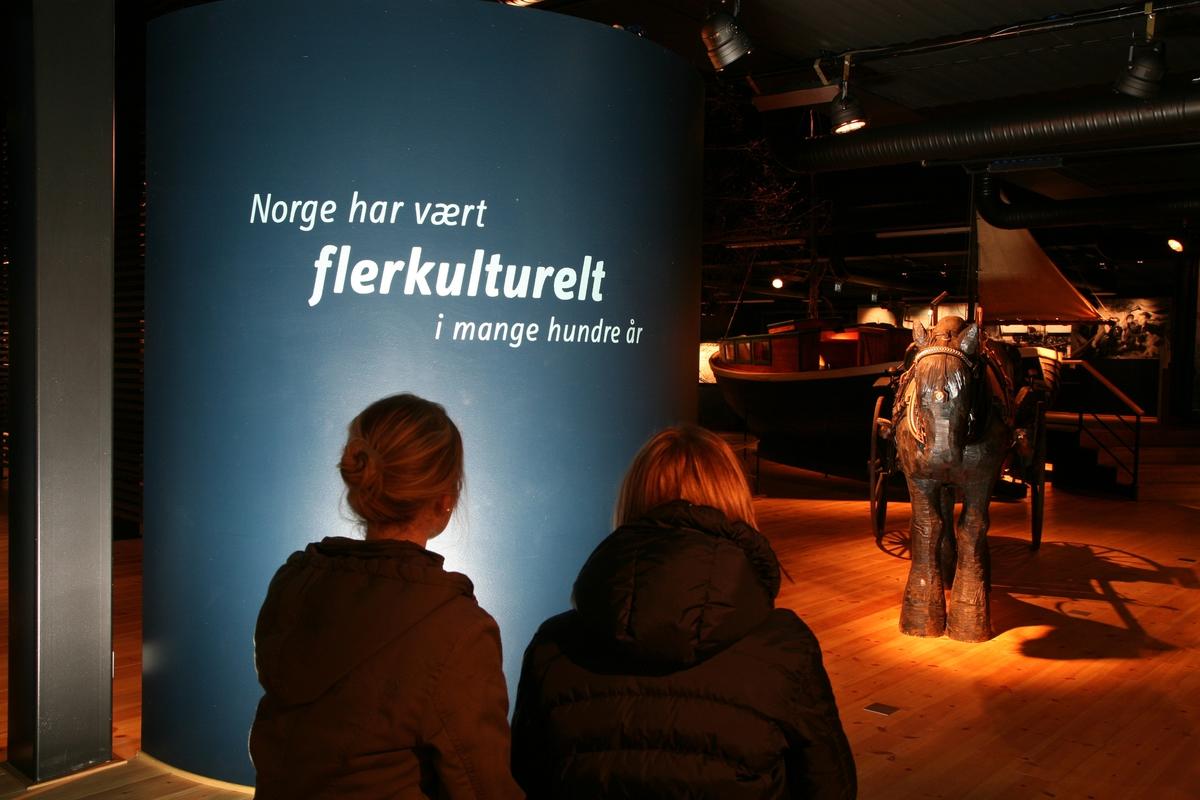 To personer som leser en utstillingstekst i utstillingen Latjo drom. Teksten sier: Norge har vært flerkulturelt i mange hundre år.