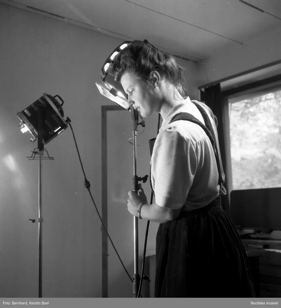 Fotografen Kerstin Bernhard riktar en lampa i sin ateljé, ca 1945. Självporträtt.