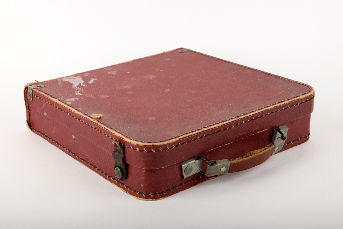 Burgunderrød koffert. Har vært brukt til oppbevaring av grammofonplater. 
Kofferten har bærehank, samt lukkemekanisme på to av sidene.
