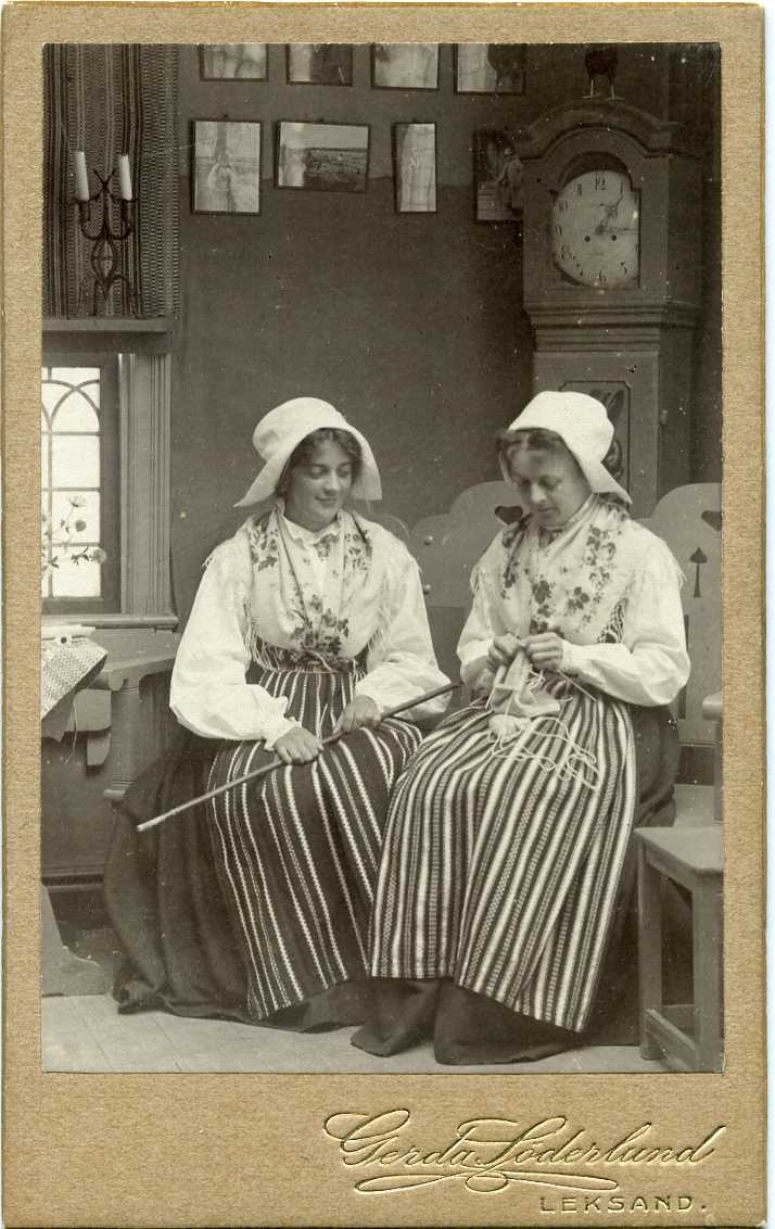 Kabinettsfotografi: troligen Anna Wahlström el Anna Wågenberg och okänd kvinna, sitter i en stuga i folkdräkt och en av dem stickar