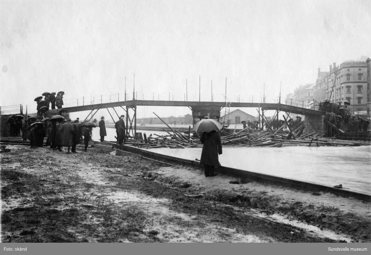 Timmerbröt ovanför gångbron (kallad Kamelryggen eller Puckelbron) i samband med den stora vårfloden 1919. Bron som låg i Norrlandsgatans förlängning raserades helt vid översvämningen. Den återuppbyggdes inte utan ersattes 1927 med den som även kallades Puckelbron i Malmskillnadsgatans förlängning.